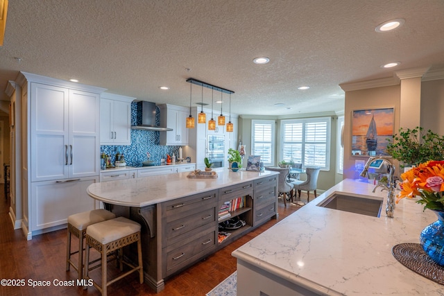 kitchen featuring white cabinetry, sink, wall chimney exhaust hood, light stone countertops, and decorative light fixtures