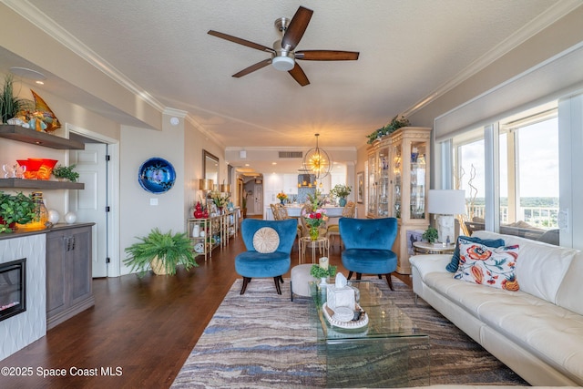 living room with ceiling fan with notable chandelier, dark hardwood / wood-style floors, ornamental molding, and a textured ceiling