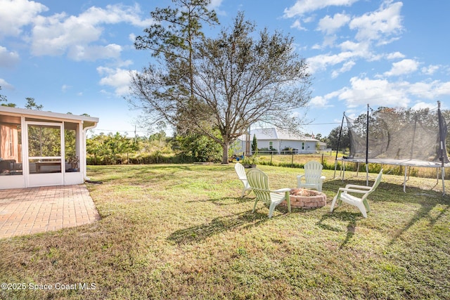 view of yard with a trampoline, an outdoor fire pit, and a sunroom