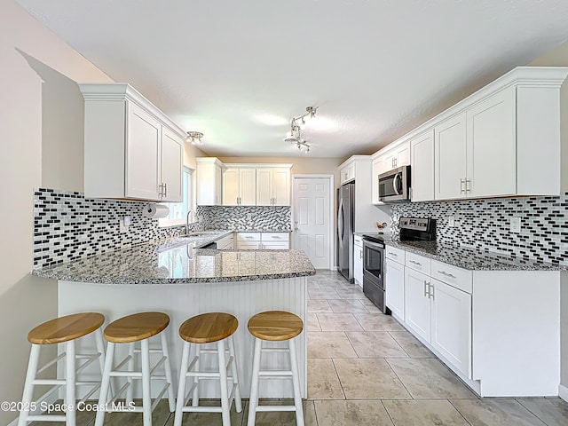 kitchen with a peninsula, stone counters, decorative backsplash, and appliances with stainless steel finishes