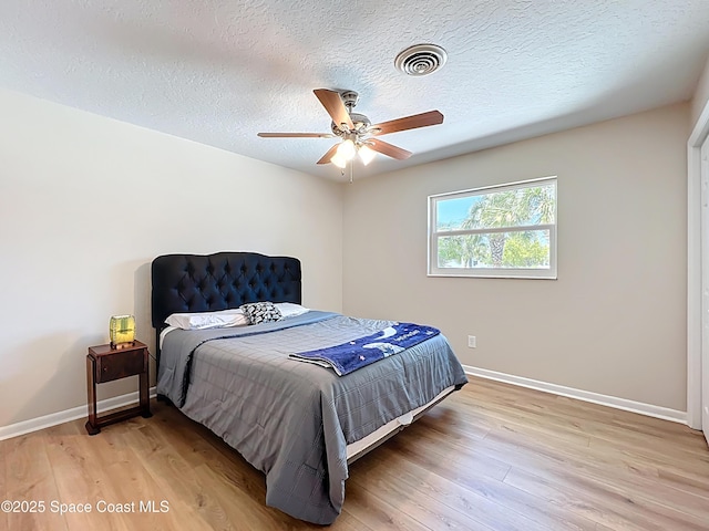 bedroom with baseboards, a textured ceiling, visible vents, and light wood-type flooring