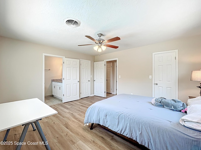 bedroom with visible vents, a ceiling fan, light wood-style floors, baseboards, and ensuite bathroom