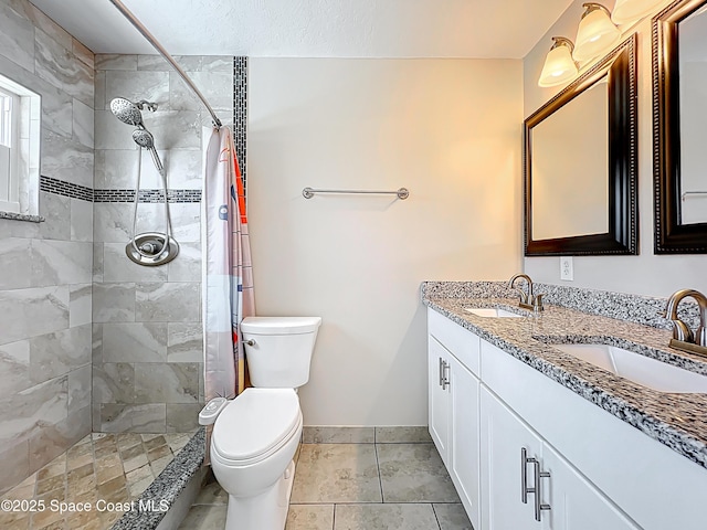 bathroom featuring a tile shower, toilet, a sink, and double vanity