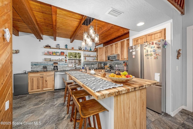 kitchen featuring hanging light fixtures, a kitchen island, butcher block countertops, appliances with stainless steel finishes, and beamed ceiling