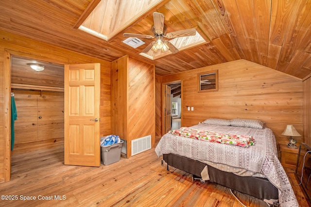 bedroom featuring wooden ceiling, hardwood / wood-style floors, ceiling fan, wood walls, and vaulted ceiling with skylight