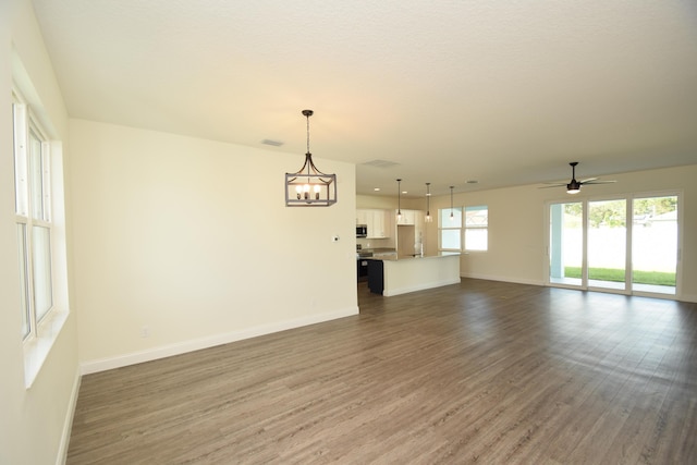 unfurnished living room featuring dark wood-type flooring and ceiling fan with notable chandelier