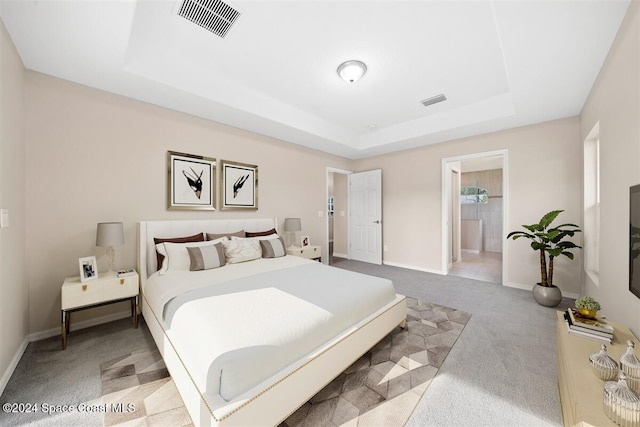 bedroom with a raised ceiling, ensuite bath, and light carpet