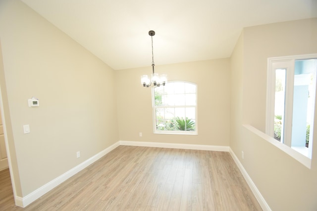 spare room with a wealth of natural light, a chandelier, and light wood-type flooring