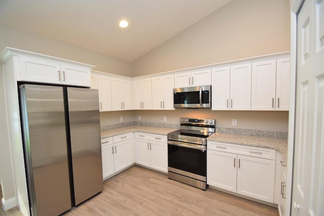 kitchen featuring lofted ceiling, white cabinets, light stone countertops, light hardwood / wood-style floors, and stainless steel appliances