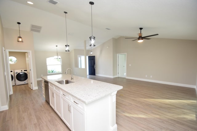 kitchen featuring white cabinets, sink, washer and dryer, an island with sink, and light stone counters