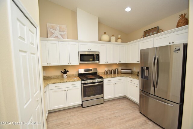 kitchen featuring appliances with stainless steel finishes, light stone counters, white cabinets, light hardwood / wood-style floors, and lofted ceiling