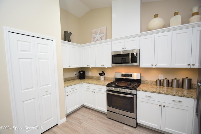 kitchen featuring white cabinetry, light stone countertops, vaulted ceiling, appliances with stainless steel finishes, and light wood-type flooring