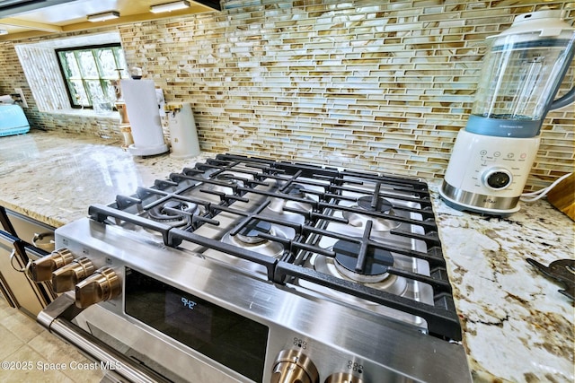 interior details with light stone countertops, decorative backsplash, and stainless steel range with gas cooktop