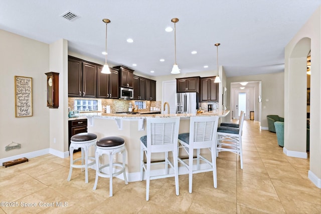 kitchen with stainless steel appliances, a kitchen breakfast bar, backsplash, an island with sink, and pendant lighting