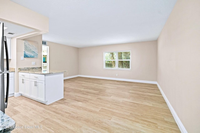 kitchen featuring stainless steel refrigerator, light stone counters, light hardwood / wood-style flooring, and white cabinets