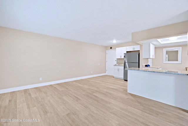 kitchen featuring light stone countertops, white cabinetry, stainless steel refrigerator, and light hardwood / wood-style flooring