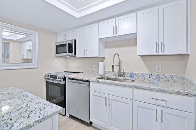 kitchen with white cabinetry, sink, light stone counters, appliances with stainless steel finishes, and light wood-type flooring