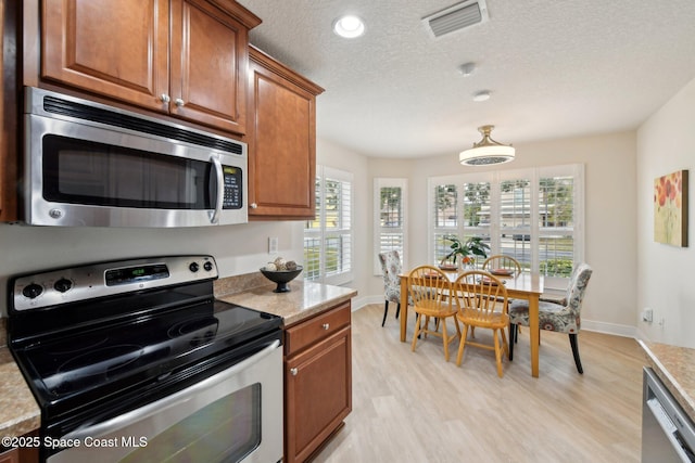 kitchen with light stone counters, appliances with stainless steel finishes, light hardwood / wood-style floors, and a textured ceiling