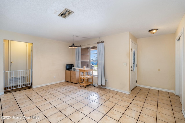 interior space featuring light tile patterned floors, baseboards, visible vents, and a textured ceiling