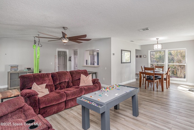 living room with ceiling fan with notable chandelier, light wood-type flooring, and a textured ceiling