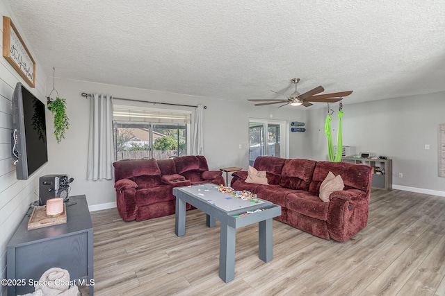 living room featuring ceiling fan, light hardwood / wood-style flooring, and a textured ceiling