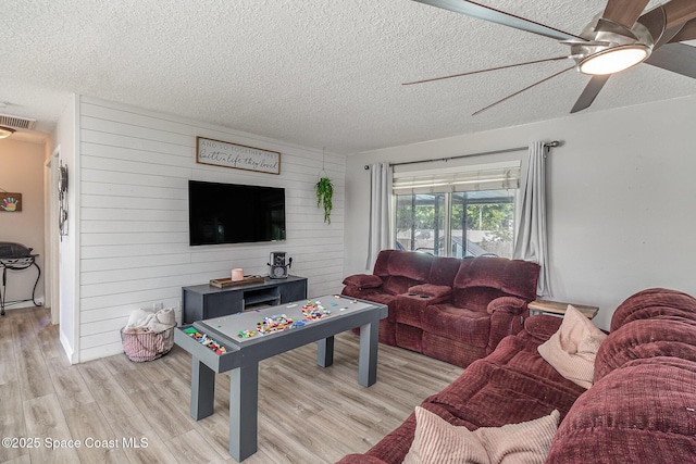 living room featuring ceiling fan, a textured ceiling, wooden walls, and light hardwood / wood-style flooring