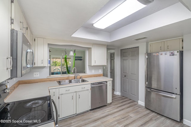 kitchen with sink, light hardwood / wood-style flooring, a tray ceiling, white cabinets, and appliances with stainless steel finishes