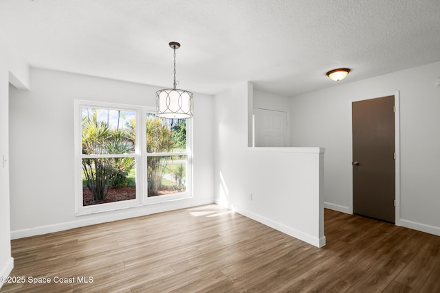 unfurnished dining area with a textured ceiling, baseboards, and wood finished floors