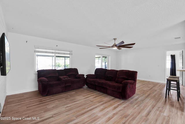 living room featuring visible vents, light wood-style flooring, a ceiling fan, a textured ceiling, and baseboards