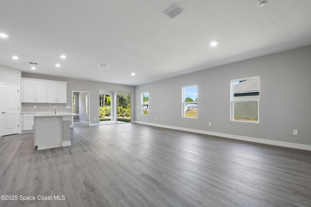 unfurnished living room featuring sink, a textured ceiling, and light wood-type flooring