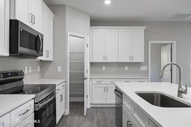 kitchen with white cabinetry, wood-type flooring, sink, backsplash, and stainless steel appliances