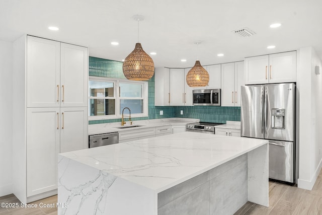 kitchen with white cabinetry, sink, stainless steel appliances, decorative light fixtures, and a kitchen island