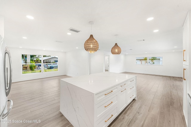 kitchen with pendant lighting, a center island, white cabinets, light wood-type flooring, and light stone countertops