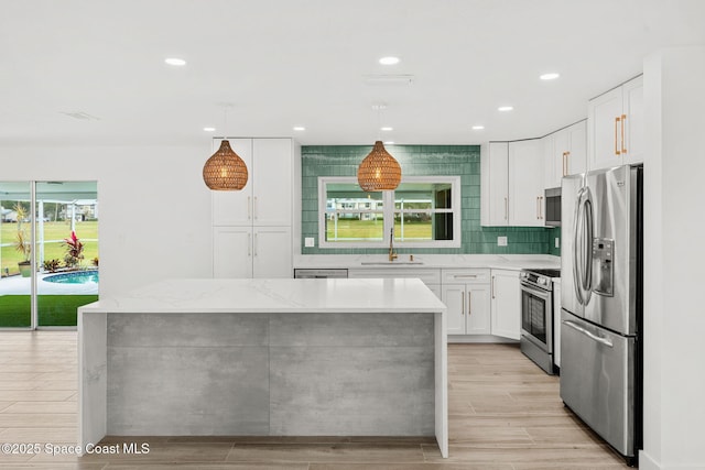 kitchen with white cabinetry, sink, stainless steel appliances, light stone counters, and pendant lighting