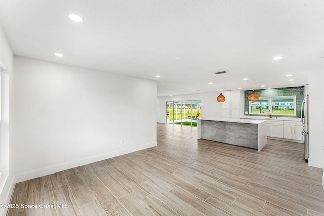 kitchen featuring a center island, stainless steel fridge, light wood-type flooring, decorative light fixtures, and white cabinetry