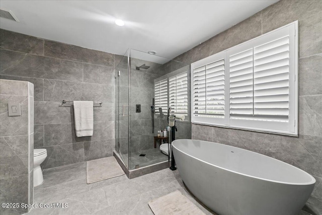 bathroom with tile patterned flooring, toilet, tile walls, and independent shower and bath