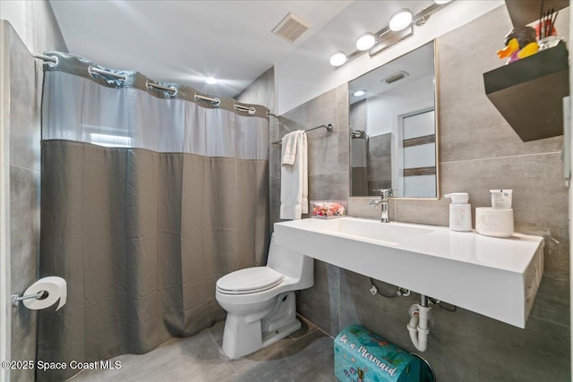 bathroom with sink, a shower with curtain, toilet, and tile walls