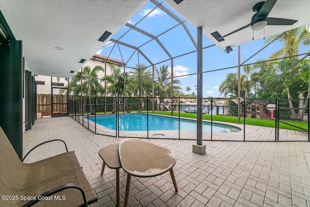 view of swimming pool with glass enclosure, ceiling fan, and a patio