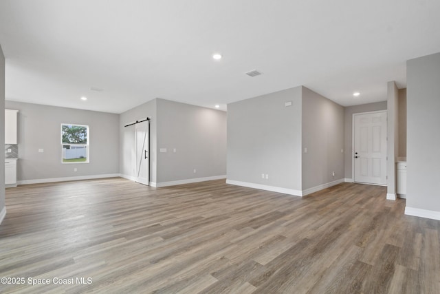 unfurnished living room featuring a barn door and light hardwood / wood-style floors