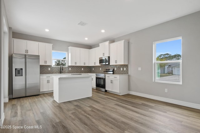 kitchen with white cabinets, stainless steel appliances, a kitchen island, and sink