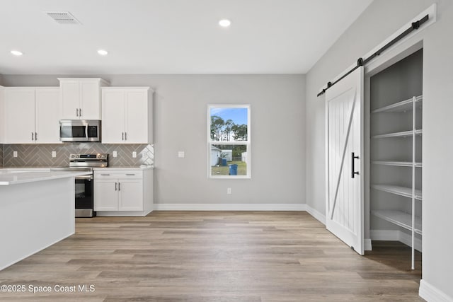 kitchen featuring a barn door, white cabinetry, light hardwood / wood-style floors, and appliances with stainless steel finishes