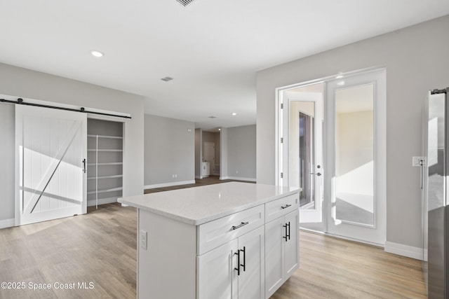 kitchen with light stone countertops, a center island, a barn door, light hardwood / wood-style floors, and white cabinets