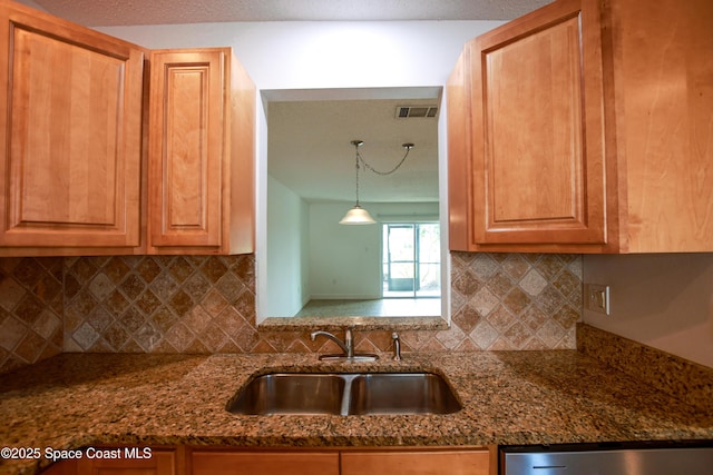 kitchen with pendant lighting, decorative backsplash, sink, and dark stone counters