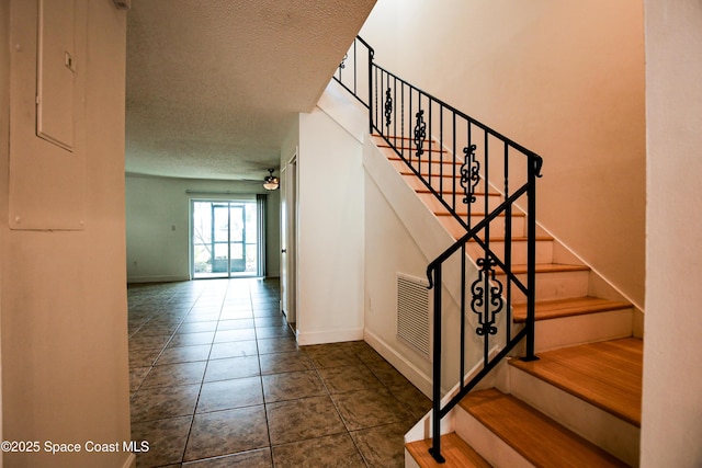 stairs with tile patterned flooring, ceiling fan, and a textured ceiling