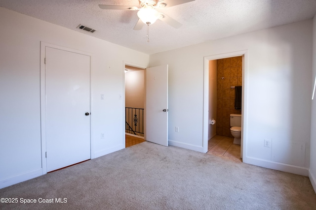 unfurnished bedroom featuring ensuite bath, ceiling fan, light colored carpet, a textured ceiling, and a closet