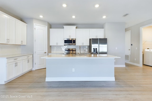 kitchen with stainless steel appliances, white cabinetry, a center island with sink, and light hardwood / wood-style flooring