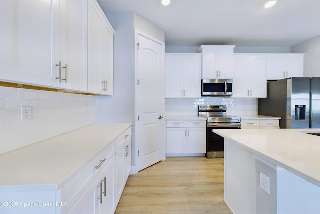 kitchen featuring backsplash, white cabinets, light hardwood / wood-style floors, and appliances with stainless steel finishes