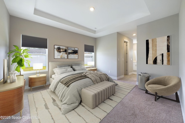 bedroom with baseboards, light colored carpet, ensuite bath, a tray ceiling, and recessed lighting