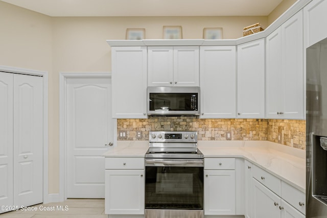 kitchen with white cabinets, decorative backsplash, light stone countertops, and appliances with stainless steel finishes