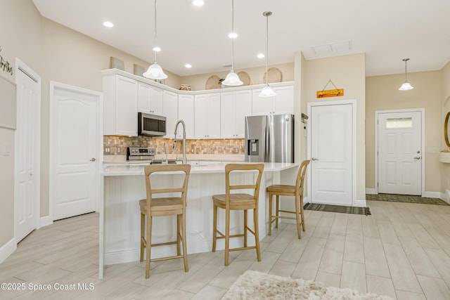 kitchen featuring tasteful backsplash, white cabinets, hanging light fixtures, and appliances with stainless steel finishes